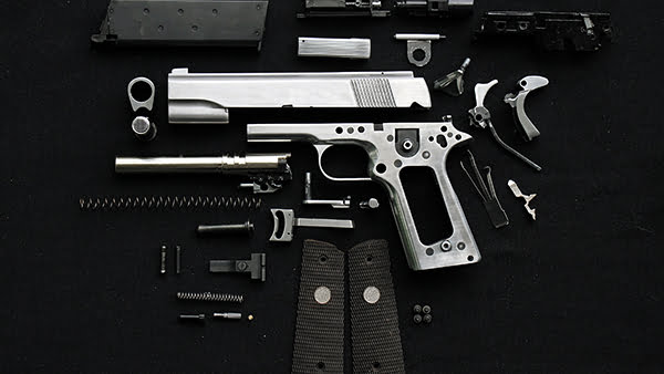 Stainless steel pistol disassembled ready to be upgraded with best firearm accessories and parts laid out on the work bench.