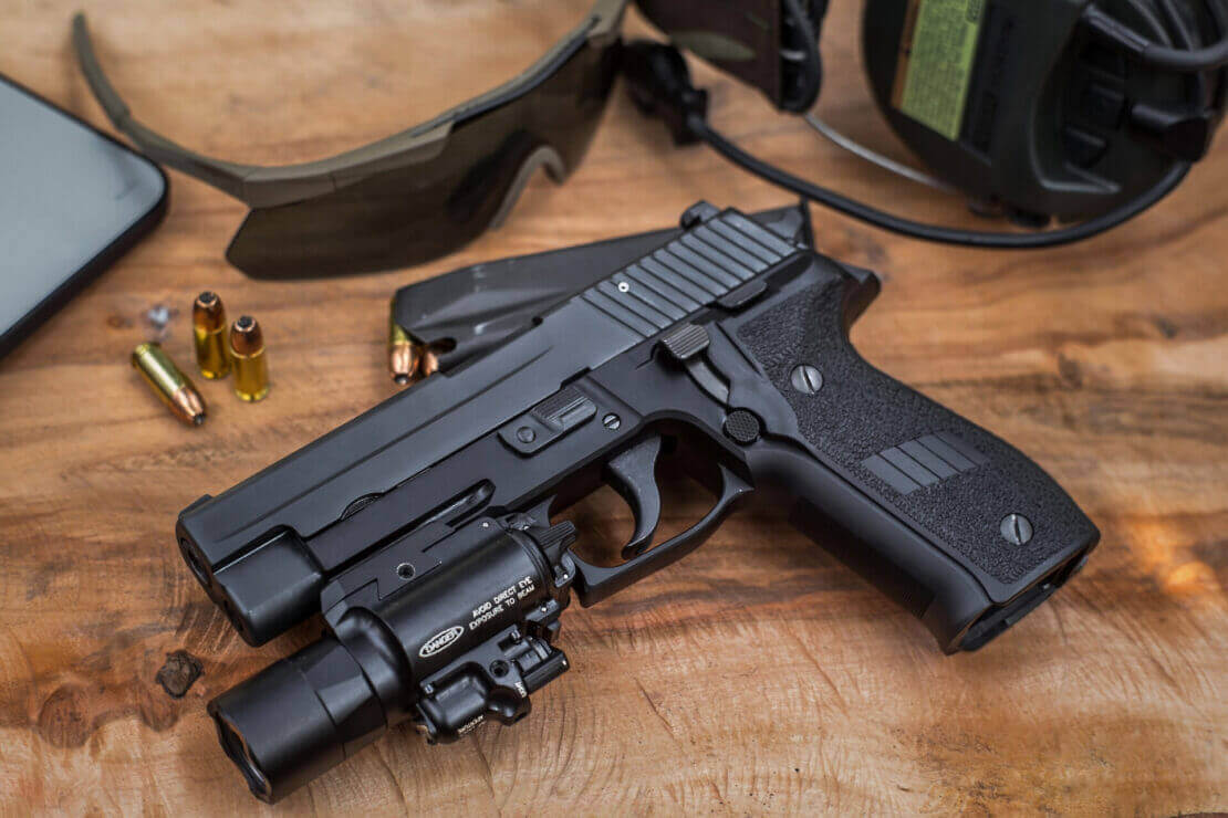 Black pistol with tactical NDZ firearm accessories on a wooden surface, surrounded by ammo and shooting gear.