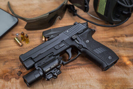 Customized 9mm handgun, pistol, firearm laying on a wood block with ear and eye protection next to a magazine and loose bullets.