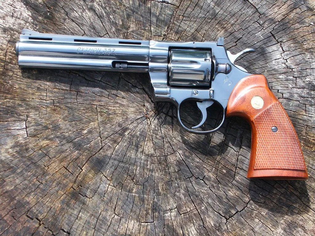 A Colt Python .357 Magnum revolver resting on a weathered wooden stump, with a focus on its wooden grips and metallic finish.