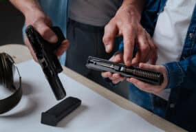 Two individuals discussing handgun upgrades while examining a disassembled handgun, focusing on the slide and internal components