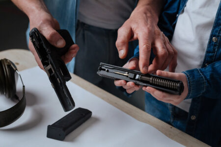 Two individuals discussing handgun upgrades while examining a disassembled handgun, focusing on the slide and internal components