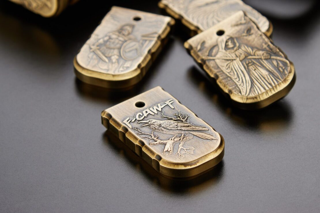 Close view of brass 3D magazine plates engraved with a raven, a reaper and a warrior