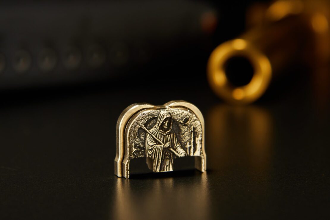 Brass 3D rear plate engraved with a hooded reaper, lit against black with a blurred brass ring behind