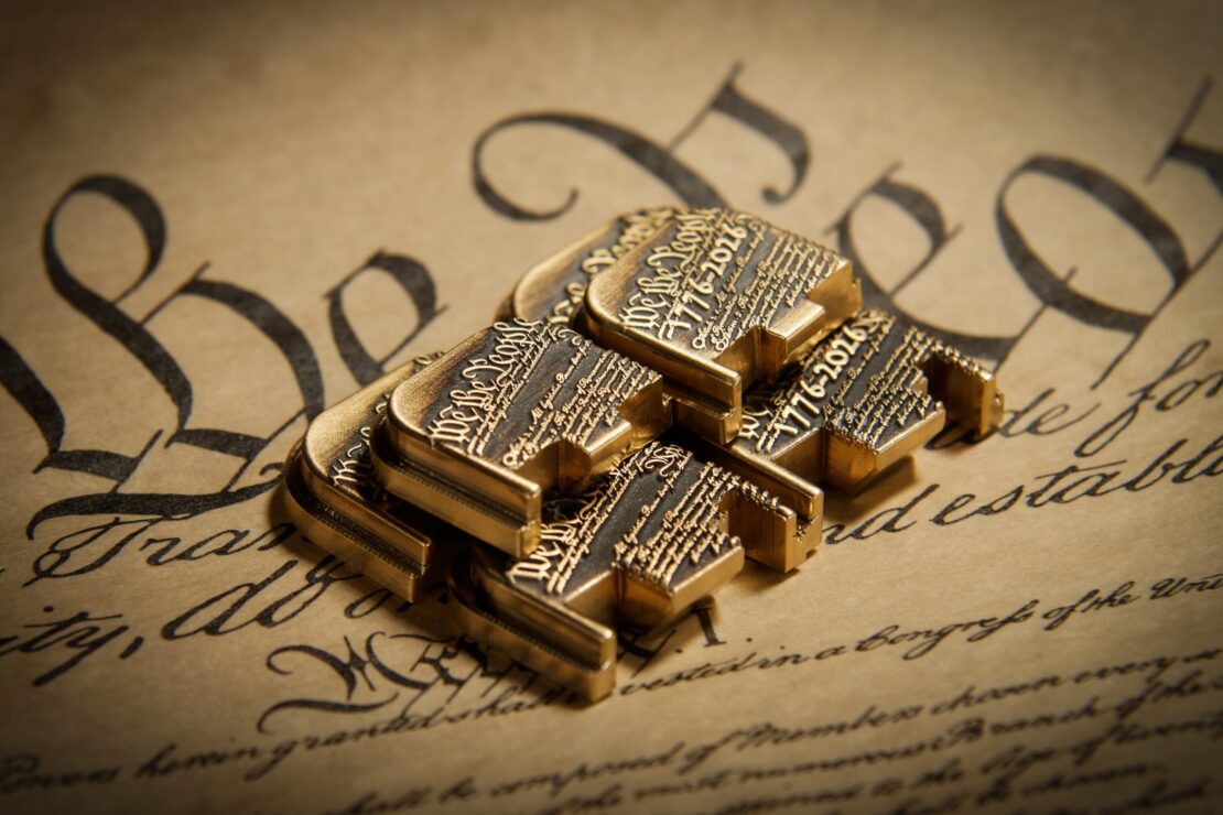 Stack of brass rear plates engraved We the People 1776-2026 on a copy of the Constitution